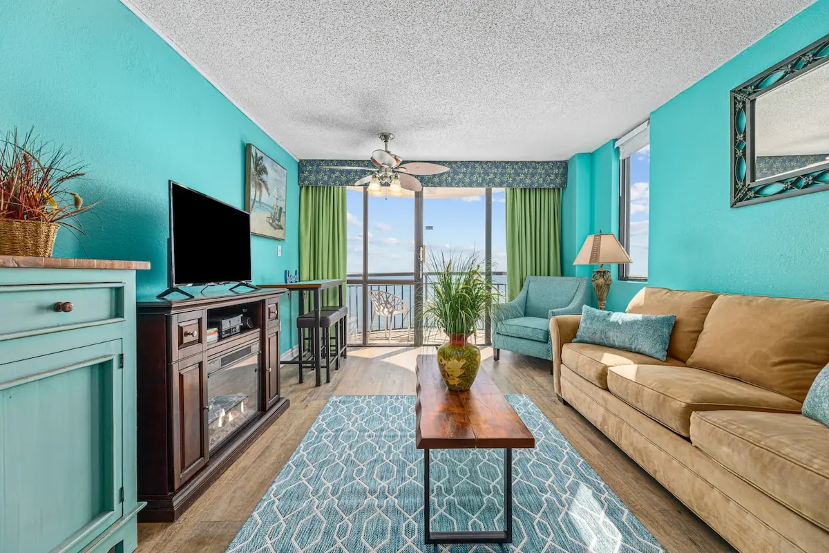 Turquoise living room with a sofa, television, and balcony doors