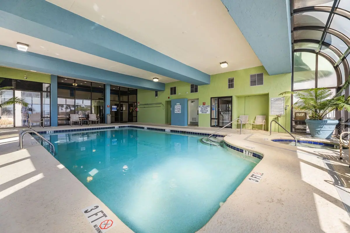 Indoor pool with lounge chairs beneath a tall windowed roof