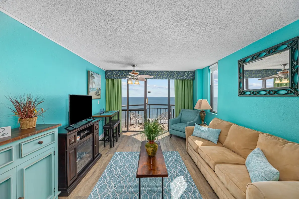 Turquoise living room with a sofa, armchair, and balcony beyond