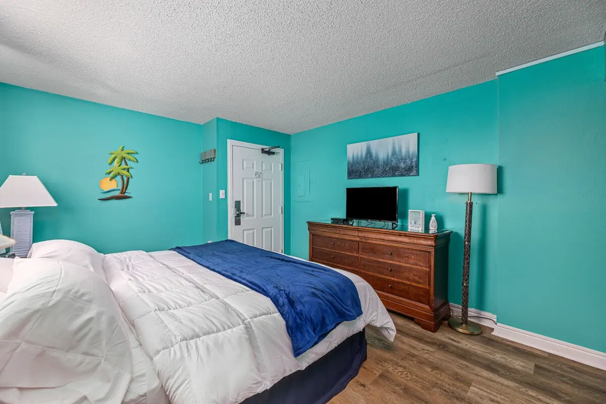 Bedroom with white bed, wood dresser, and television