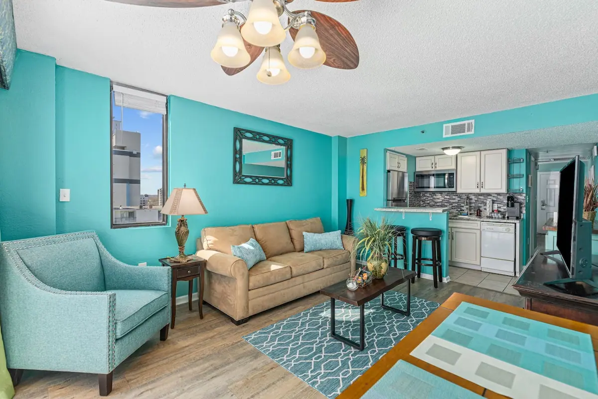 Living room with beige sofa and blue armchair facing the kitchenette