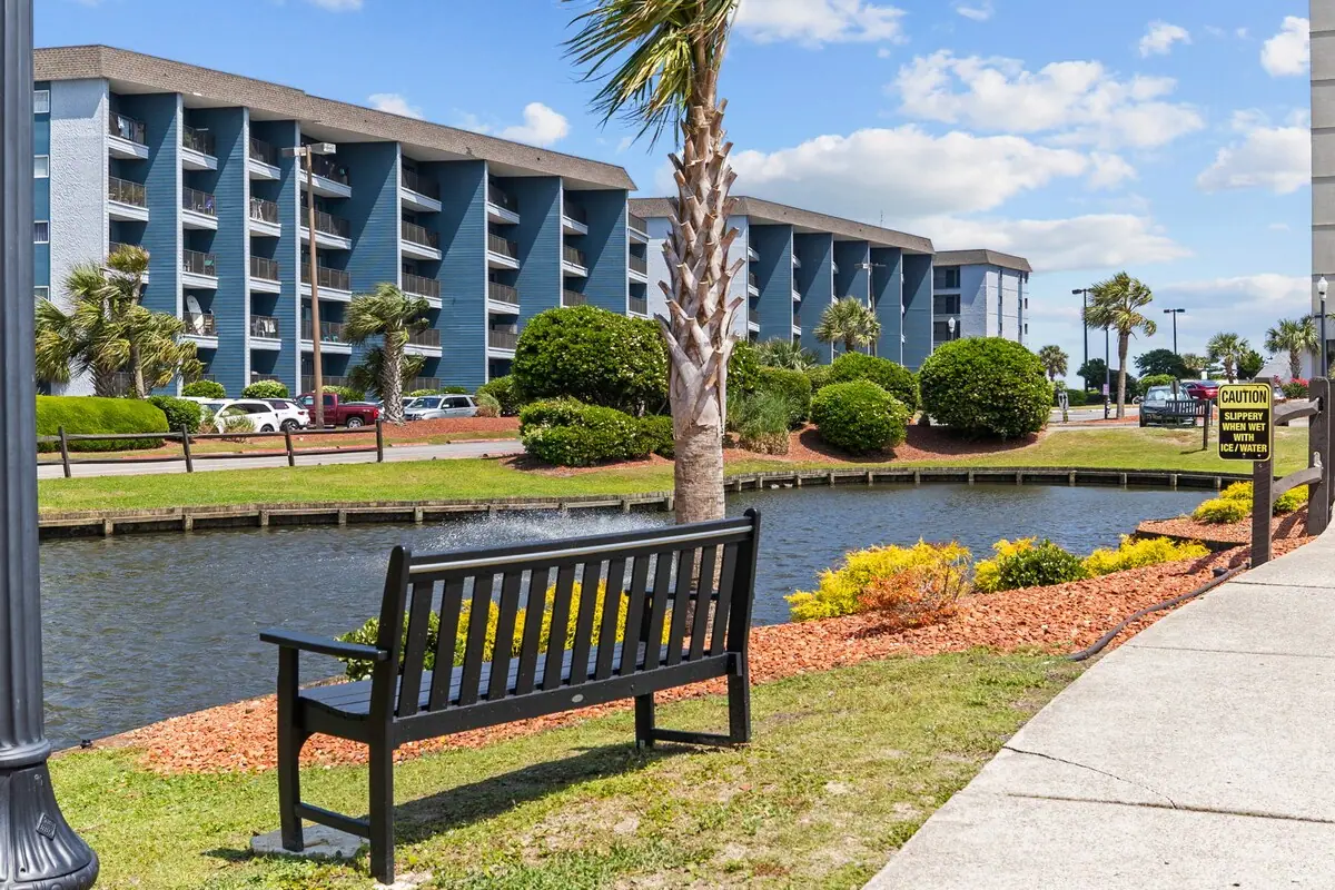 Bench beside a landscaped pond and walkway in front of condo buildings