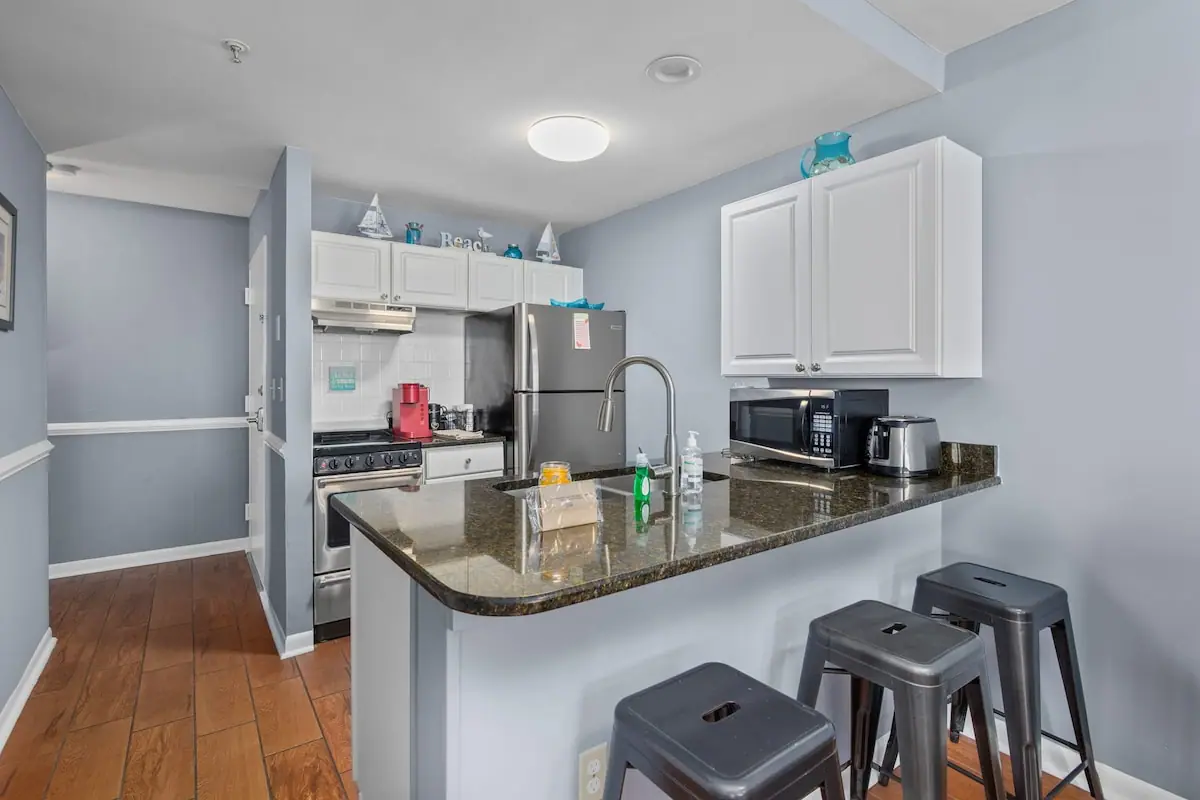 White kitchen with dark counters, breakfast bar stools, and stainless refrigerator
