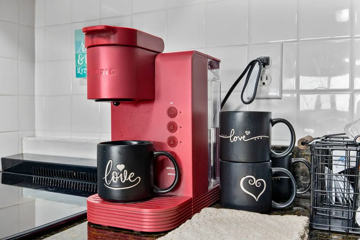 Red single-serve coffee maker and black mugs on a kitchen counter