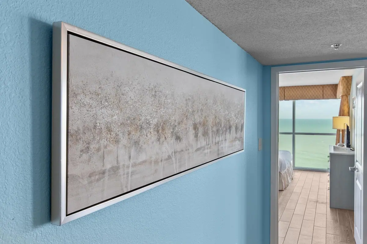 Blue hallway wall with framed art and a bedroom through the doorway