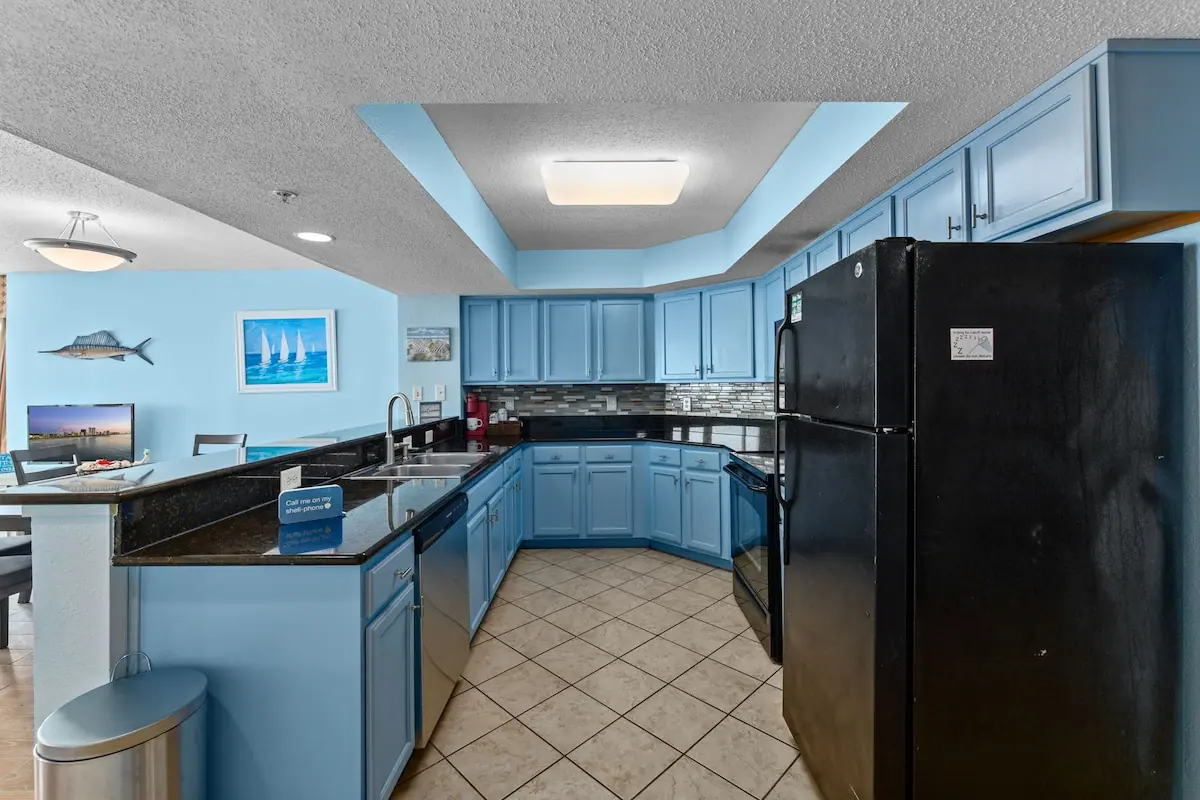 Galley kitchen with blue cabinets, black refrigerator, and breakfast counter