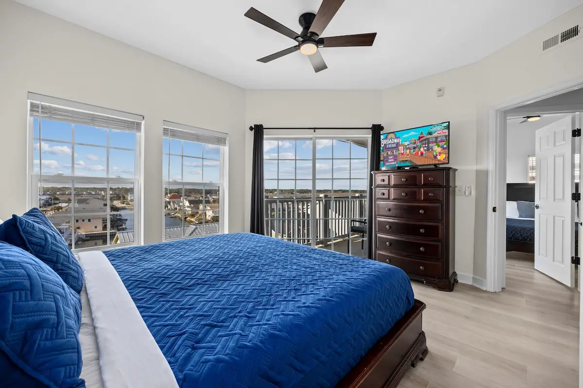 Bedroom with a blue quilt, windows, and a door to a balcony