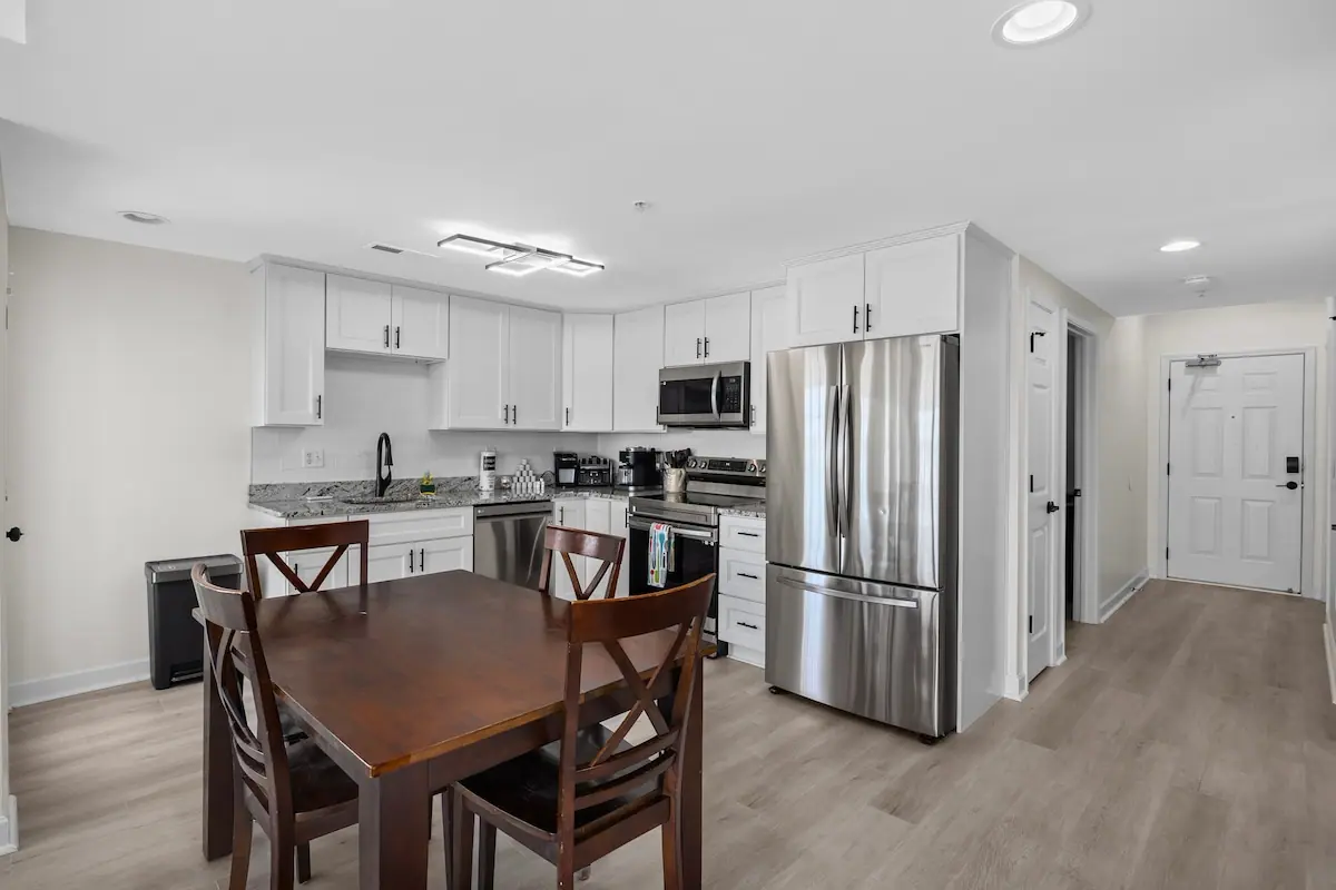 Wooden dining table in front of a white kitchen with stainless appliances
