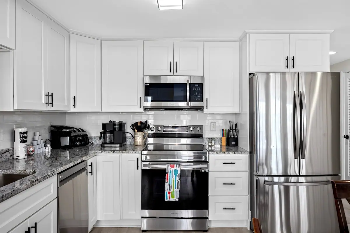 White kitchen cabinets around a stainless stove, microwave, and refrigerator