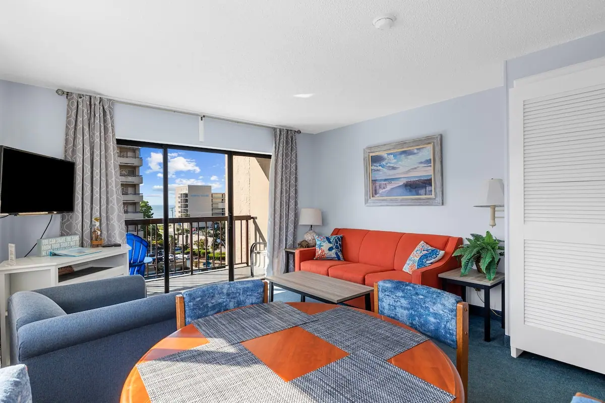 Living area with an orange sofa, dining table, and balcony doors