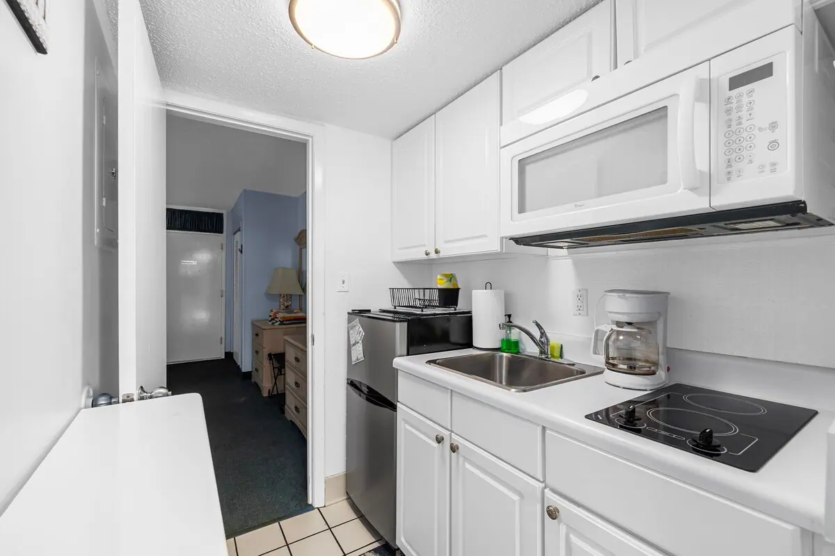 Compact white kitchenette with microwave, cooktop, sink, and refrigerator