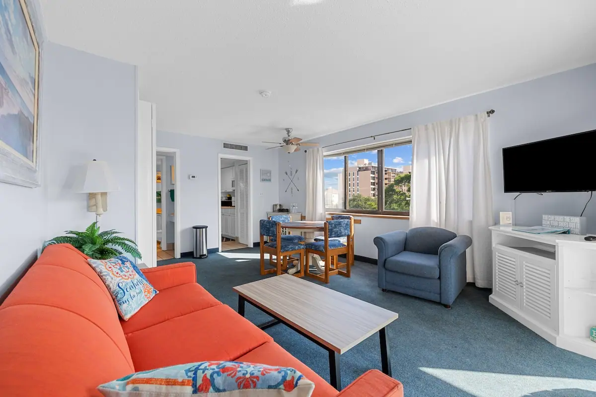 Living room with orange sofa, blue recliner, dining table, and window