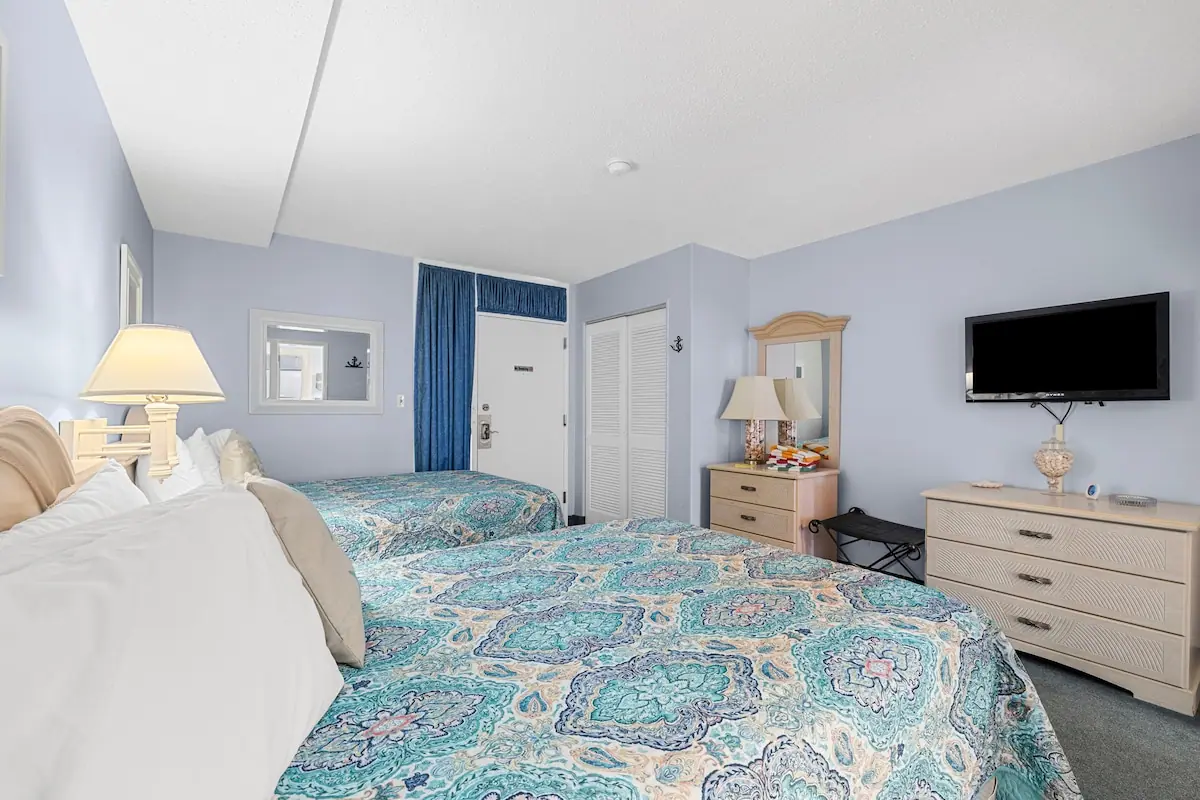 Two beds with patterned bedding, wood dresser, and wall-mounted television