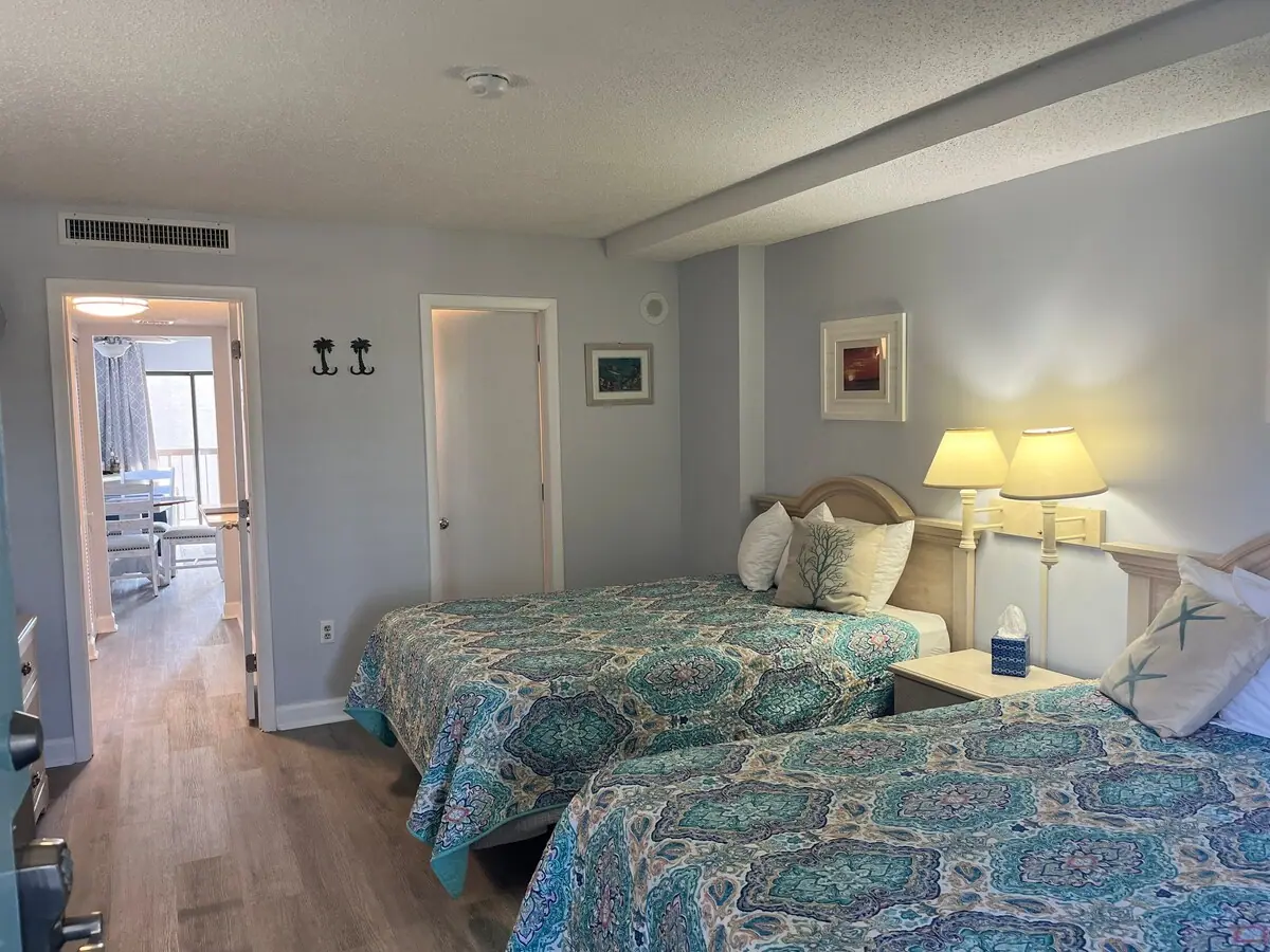 Two beds with teal bedding and a doorway toward the living room