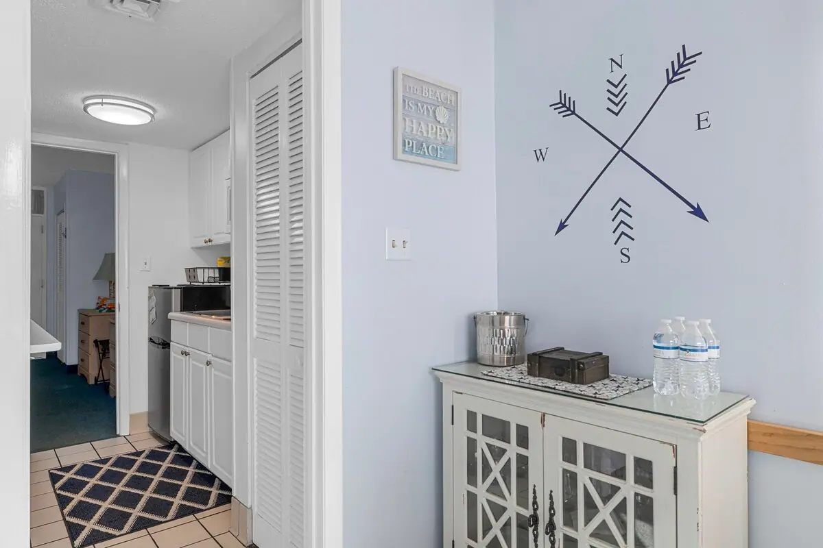 Entryway with white cabinet, compass wall art, and kitchenette beyond
