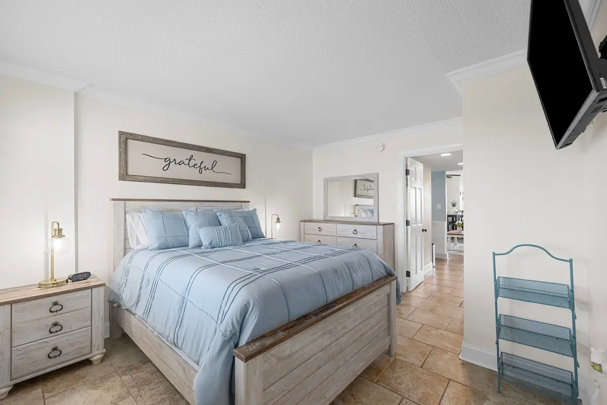 Bedroom with pale blue bedding, wood headboard, bedside lamps, and dresser