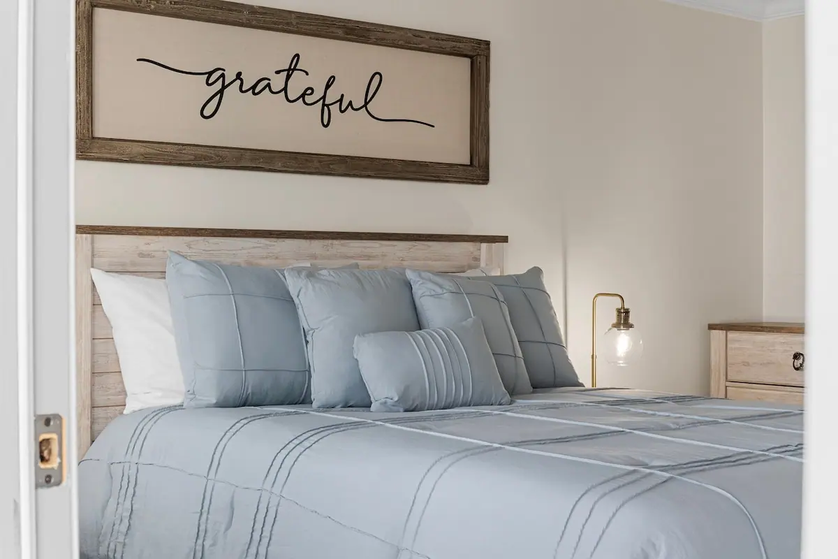 Close view of pale blue pillows and bedding beneath a wood-framed wall sign