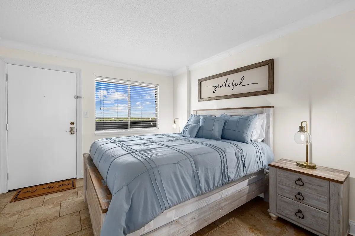 Bedroom with pale blue bedding beside a window showing blue sky
