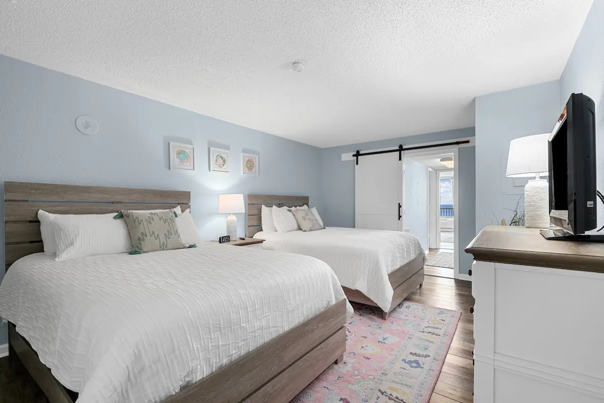 Bedroom with two white beds, a television, and a doorway toward the living area