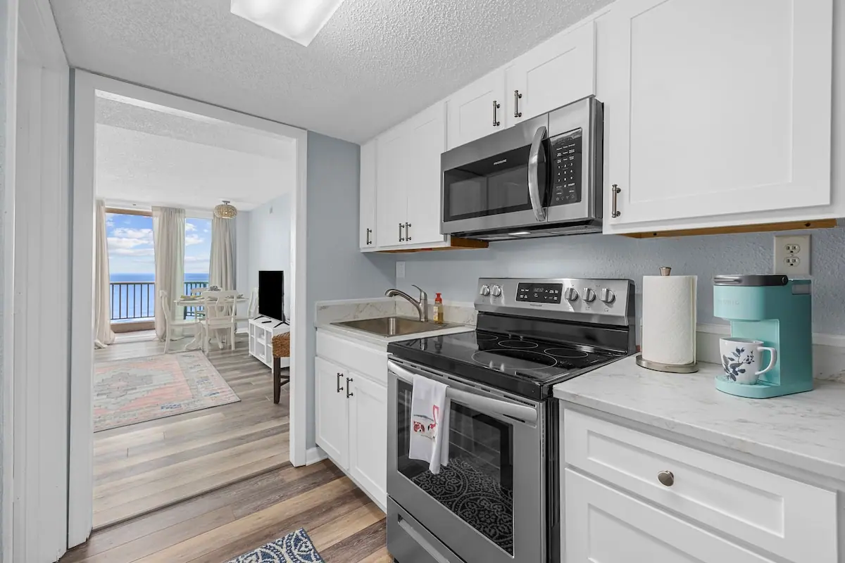 White kitchen with stove and microwave opening toward a bright living area