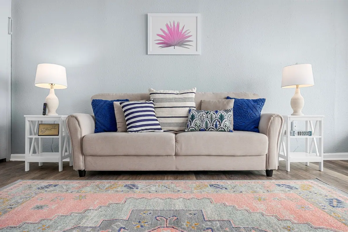Pale sofa with blue pillows between white side tables and lamps