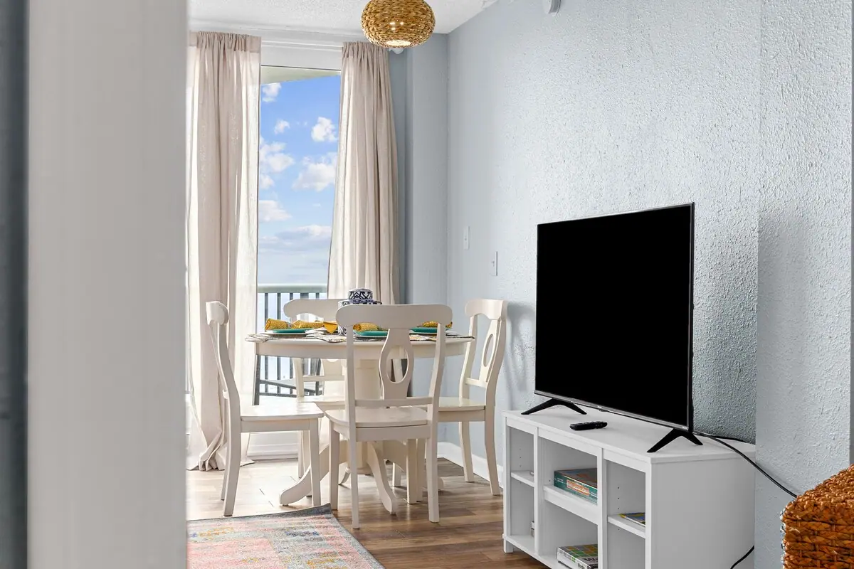 White dining table and television beside a window facing the ocean