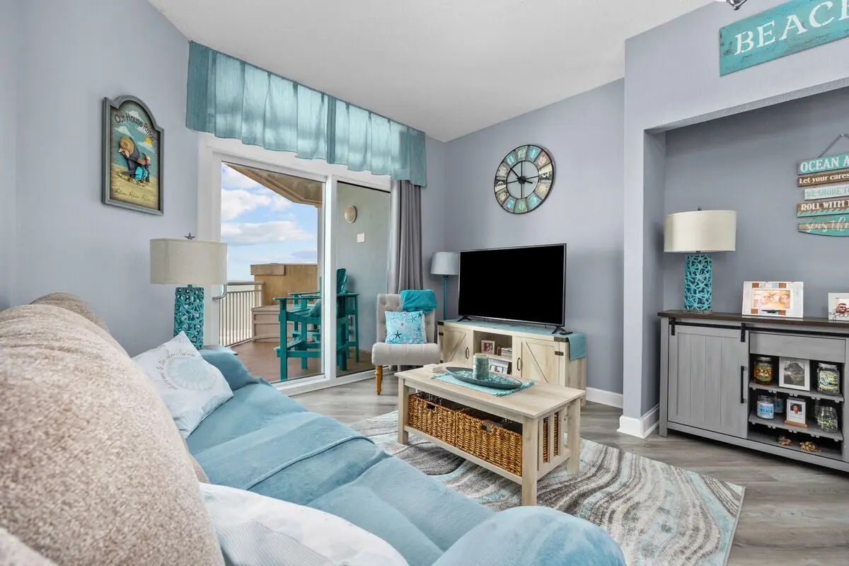 Coastal blue living room with a sofa, television, and balcony doors
