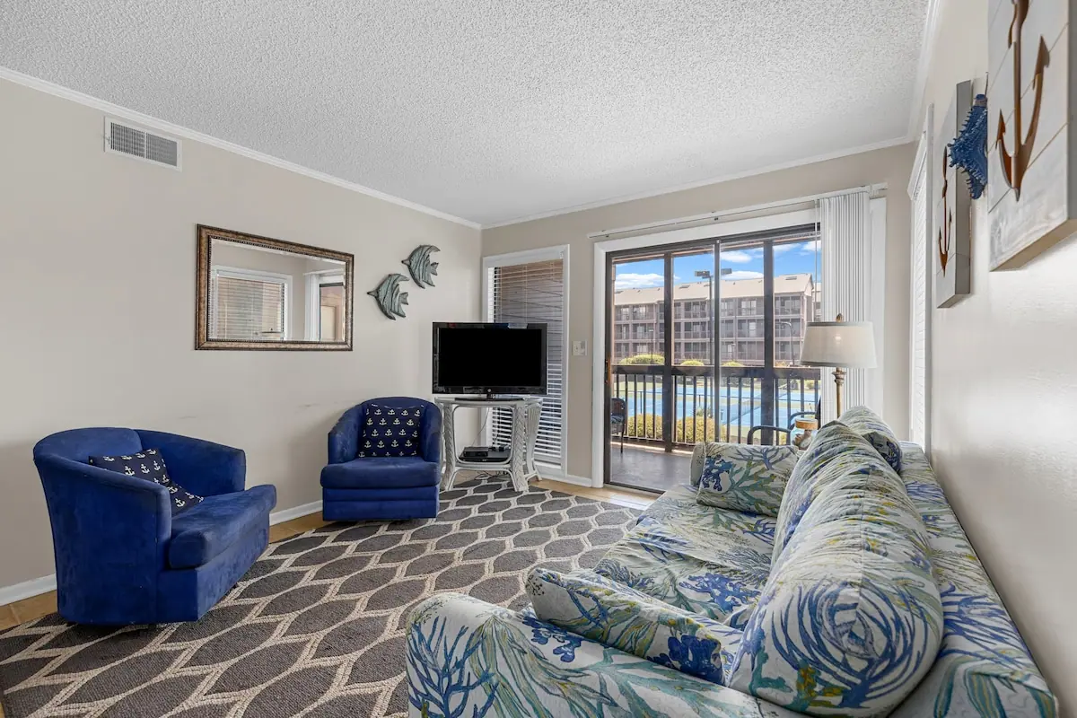 Living room with a floral sofa, blue chairs, and sliding balcony doors