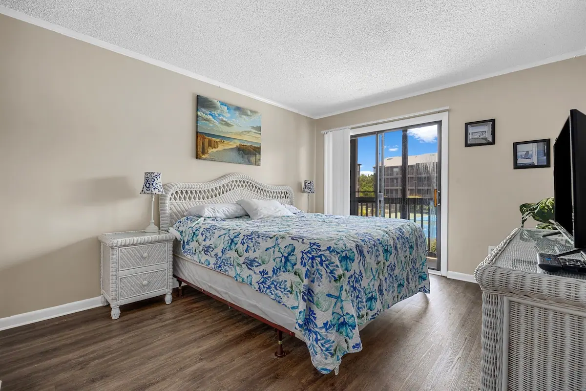 Bedroom with a blue floral bedspread and glass door to a balcony
