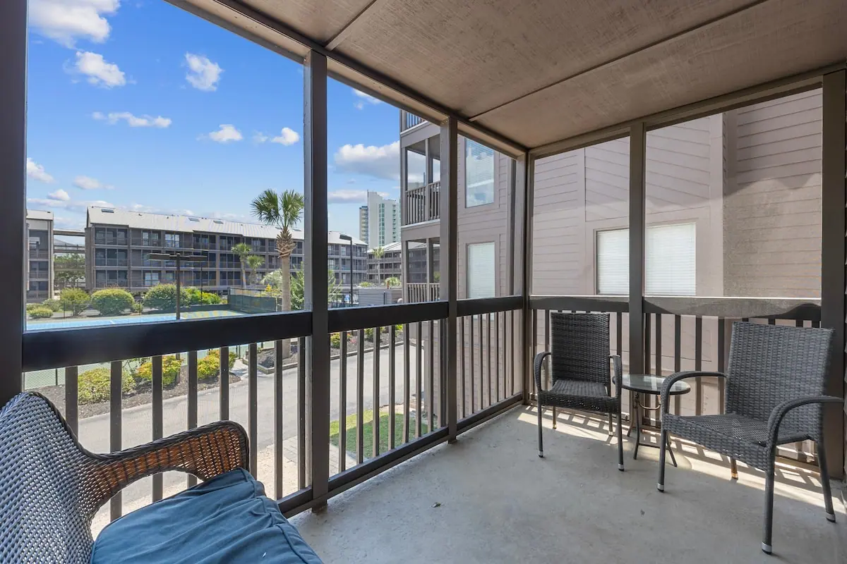 Screened balcony with chairs overlooking neighboring buildings and trees