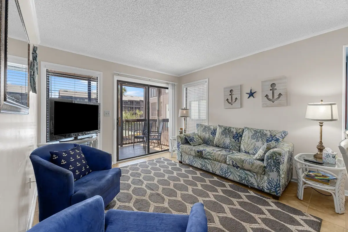 Living room with floral sofa, blue chairs, television, and balcony doors