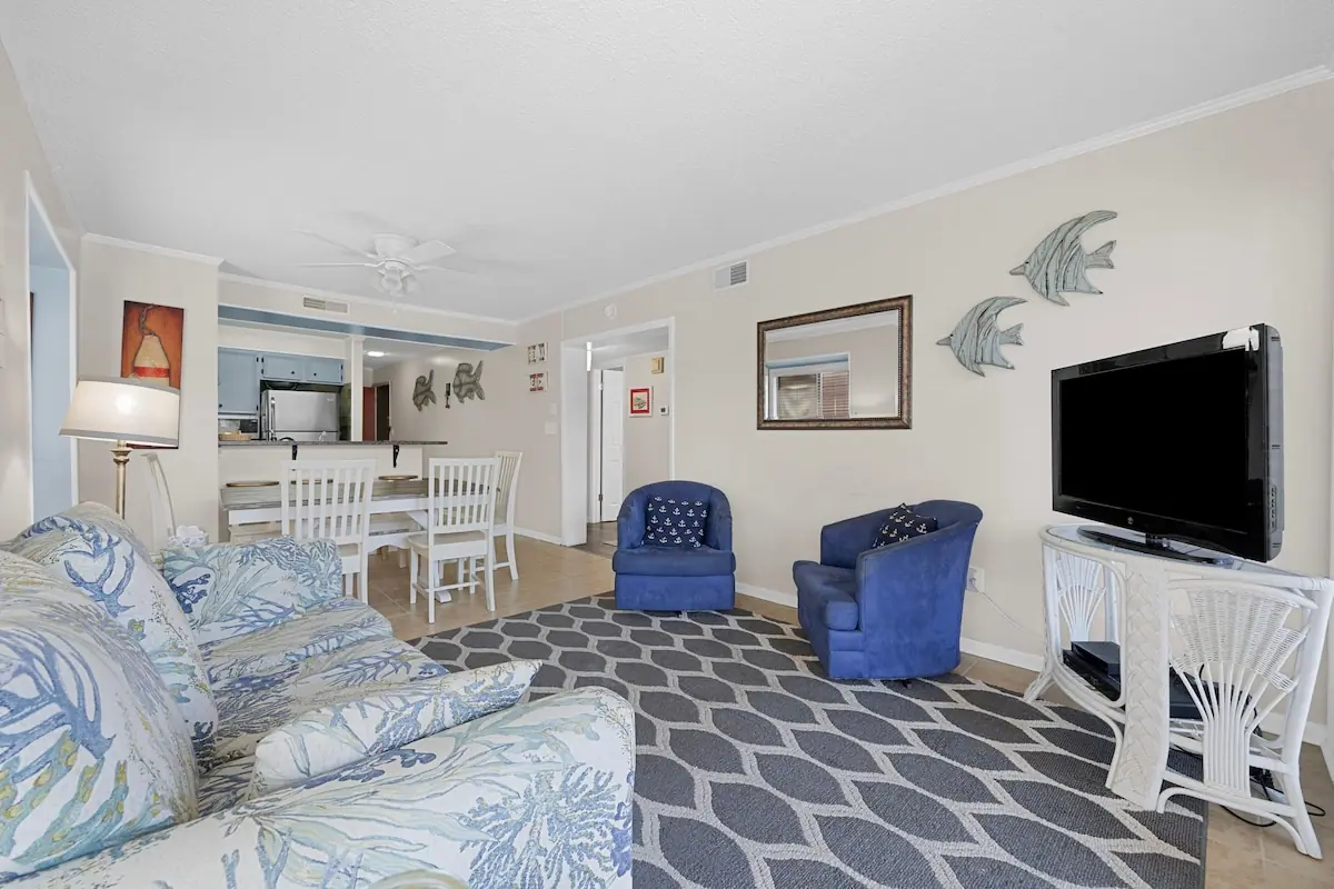 Floral sofa and blue chairs beside a white dining table and kitchen