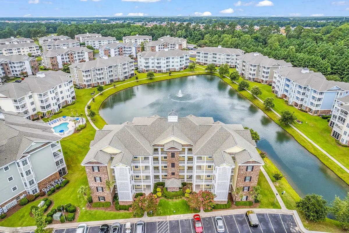 Aerial view of condo buildings around a pond with a fountain and outdoor pool