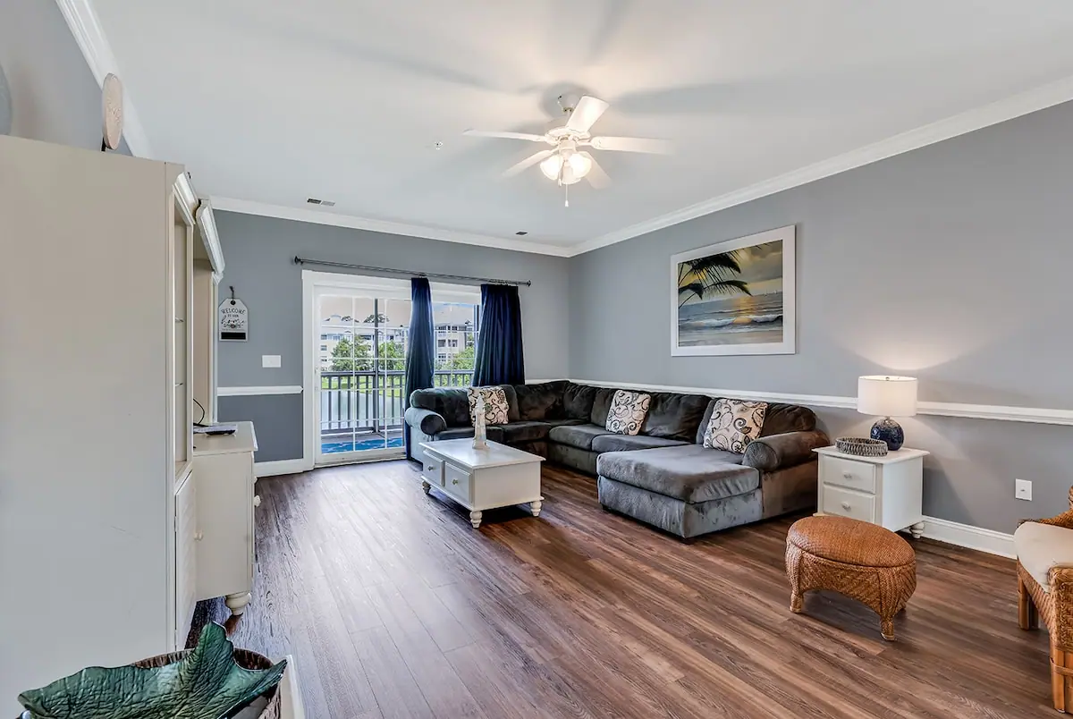 Gray sectional sofa beside glass balcony doors and beach-themed wall art