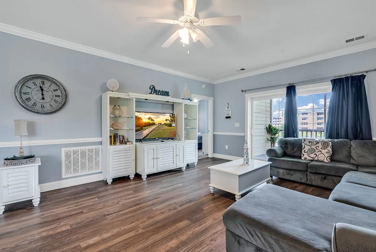 Gray sectional facing a television in a white cabinet beside balcony doors
