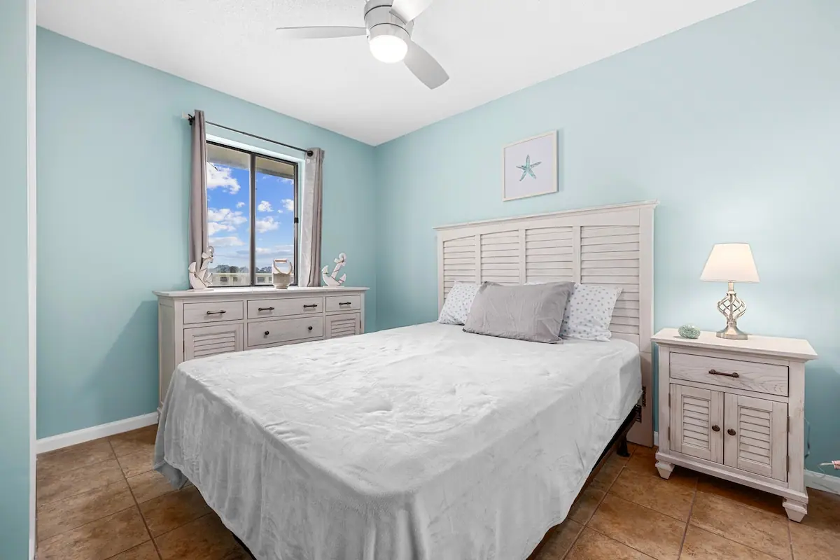 Light blue bedroom with white bed, matching nightstands, and window