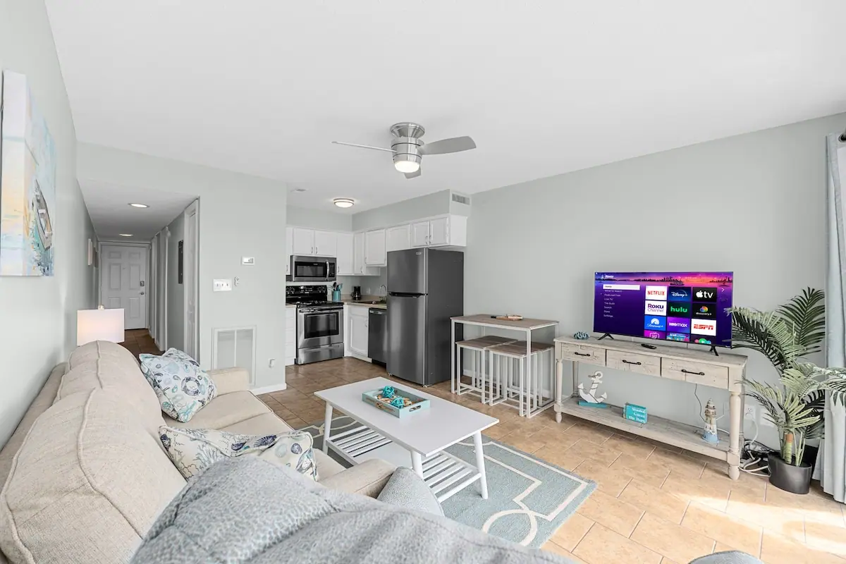 Open living room with gray sofa, television, and kitchenette