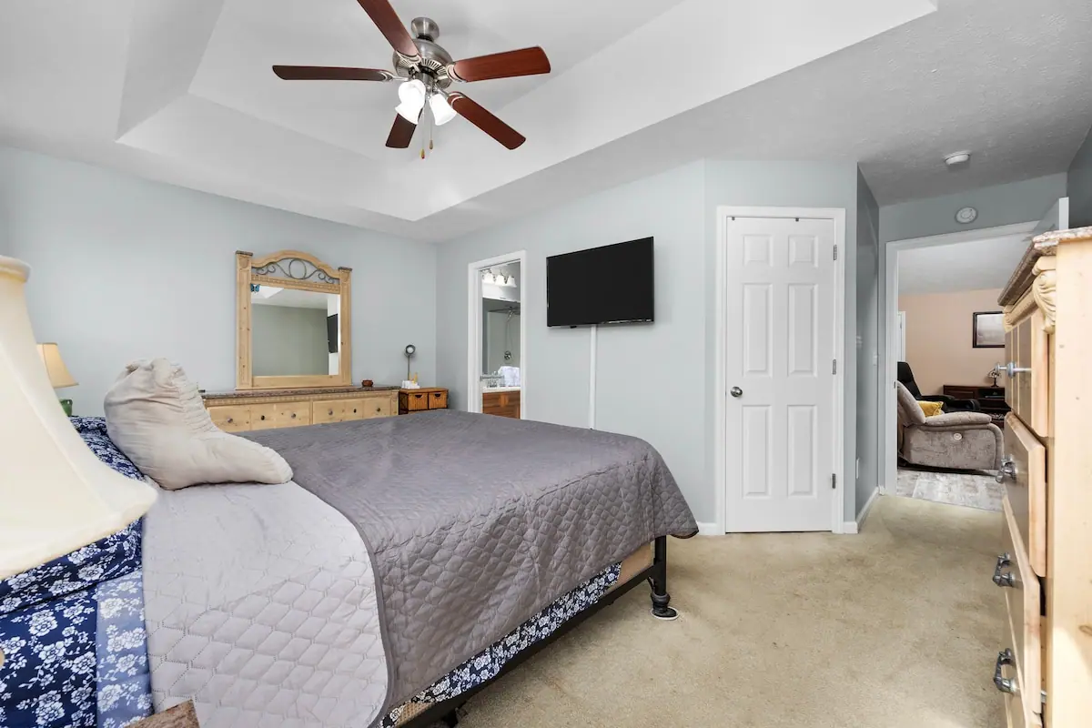 Bedroom with gray quilt, dresser, and wall-mounted TV