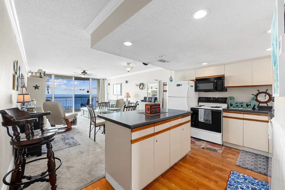 White kitchen with an island opening to a living room and ocean balcony