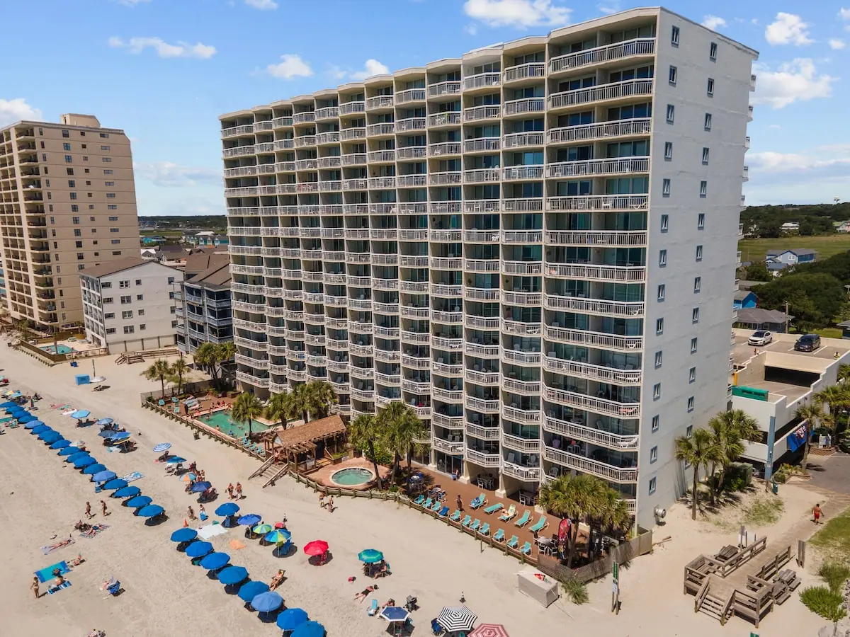 Aerial view of a beachfront building, blue beach umbrellas, and the ocean