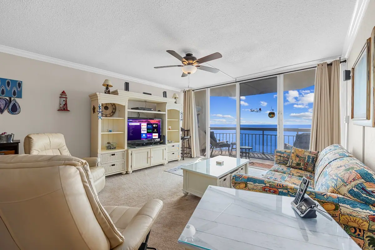 Patterned sofa and armchairs facing a television beside an ocean balcony