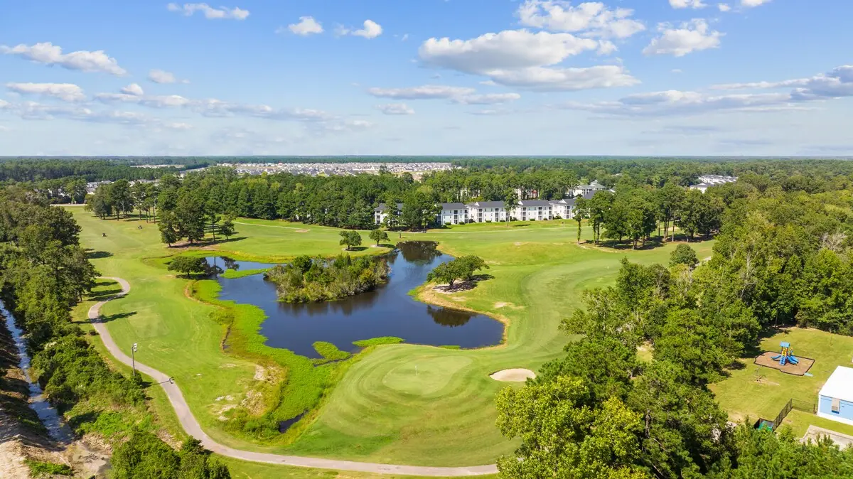 Aerial view of golf fairways curving around a pond and trees