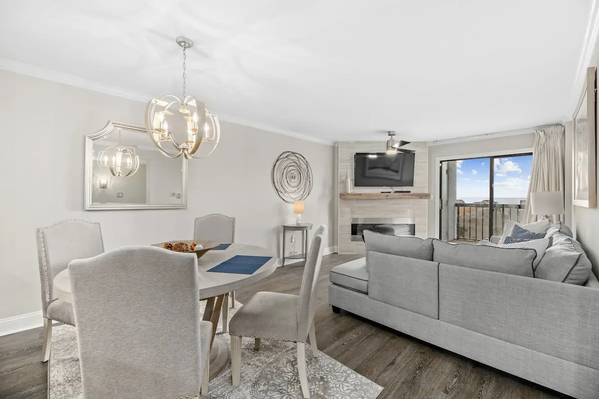 Living and dining room with gray couch, upholstered chairs, and balcony door