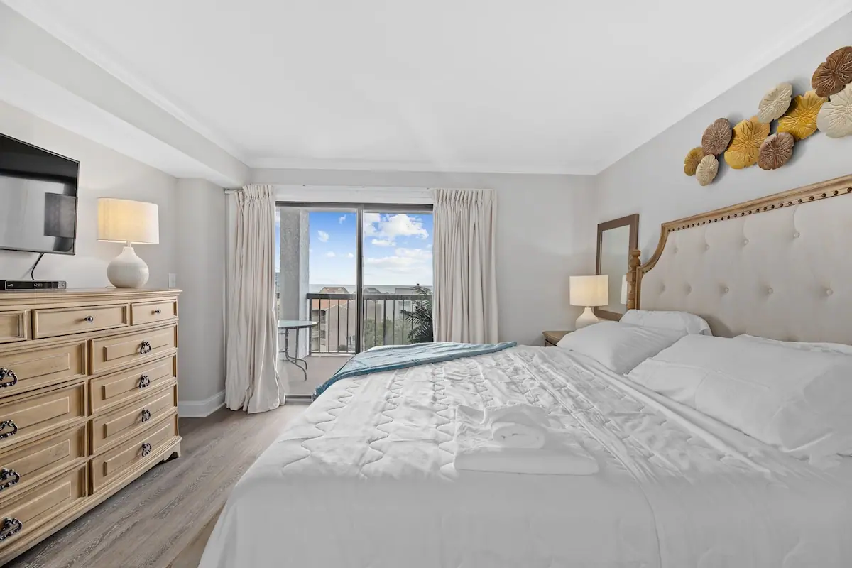 Bedroom with large white bed, wood dresser, and balcony door