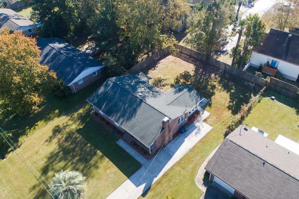 Aerial view of a single-story house with a fenced yard and surrounding trees