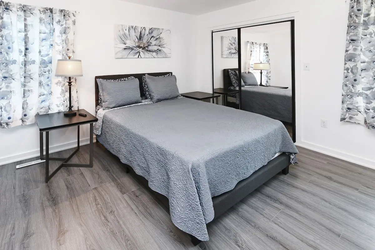 Bedroom with a gray bedspread, bedside table, and mirrored closet doors