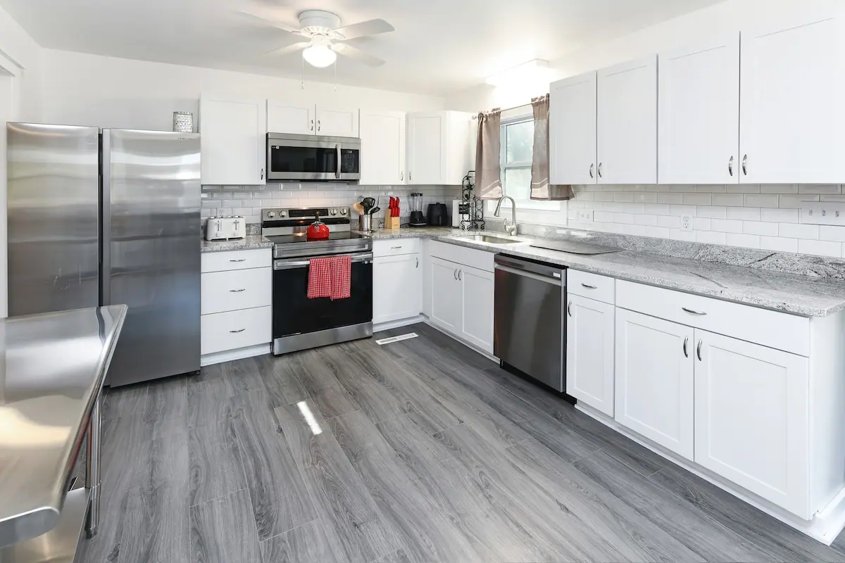 White kitchen with stainless appliances and gray wood-look flooring