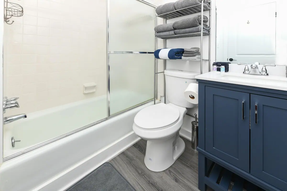 Bathroom with a tub-shower, blue vanity, and shelf of folded towels