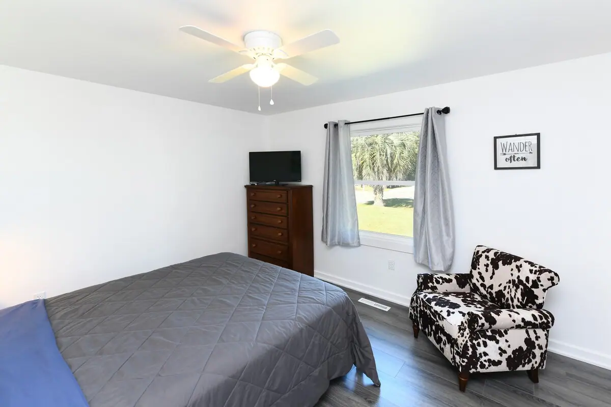 Bedroom with gray bedspread, patterned chair, and a window toward the yard