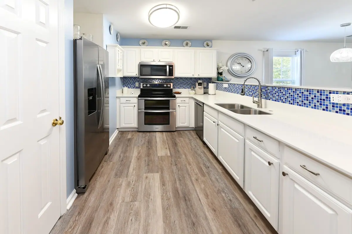 Long white kitchen with black stove, gray refrigerator, and blue tile backsplash
